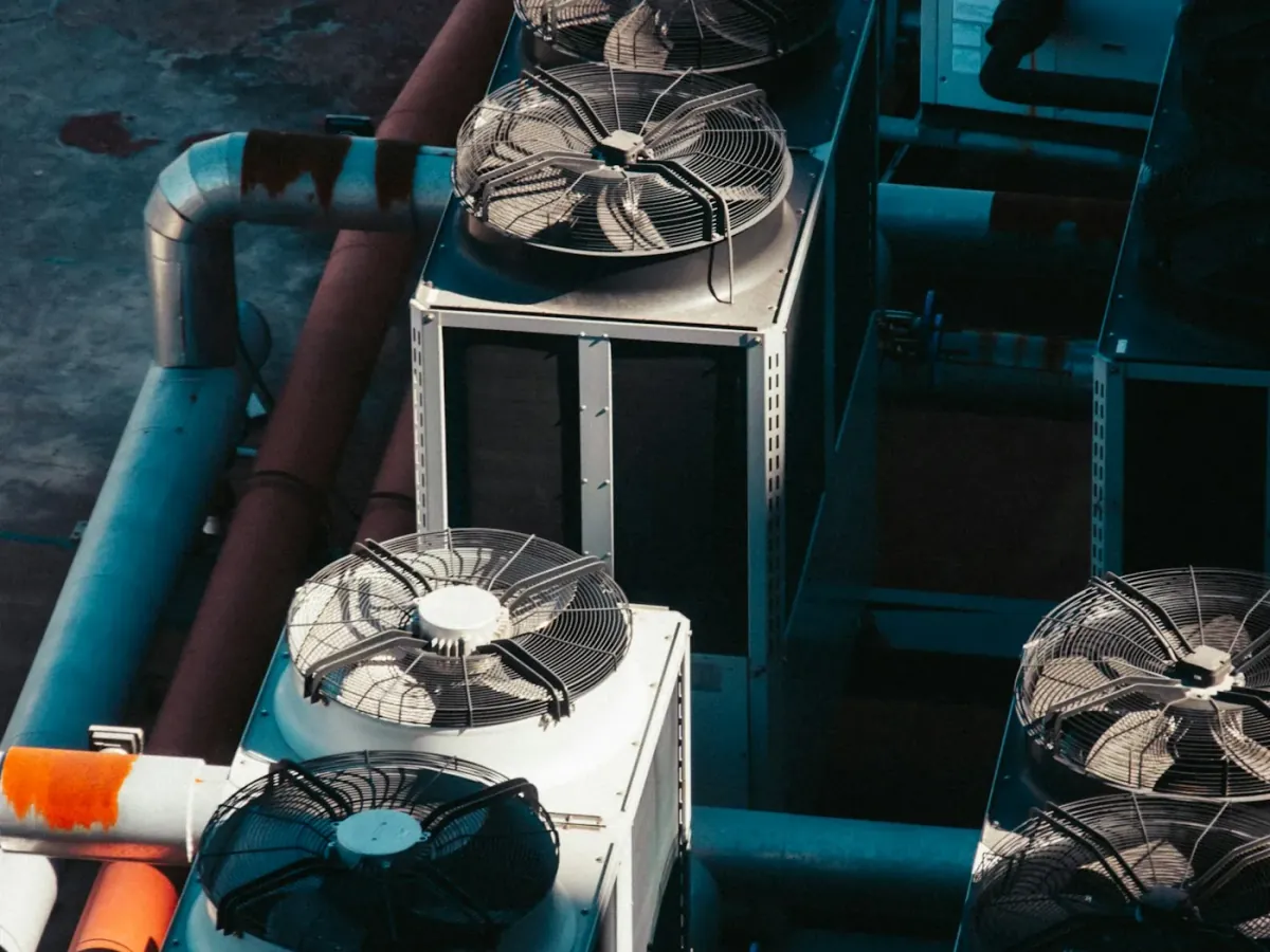 Rooftop air-cooled condenser units with exposed axial fans, seen from above beside large insulated pipes